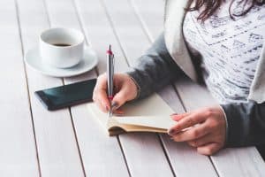 GHSC Accredited Training - person taking notes with a notepad and a cup of black coffee with a mobile phone nearby