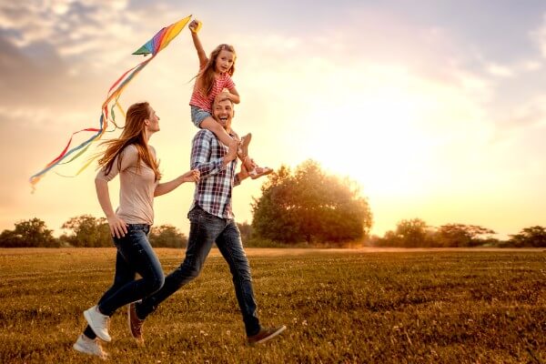 Self-care can include family time. A man with a child on his shoulders and a woman alongside.
