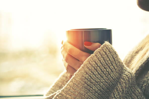 Considering whether to resist change - a person in a knitted jumper with red nails holding a drink mug.